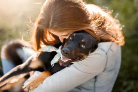 gettyimages-1034613012-e1692376010626 A woman hugging her new cute black mutt dog who was just up for adoption